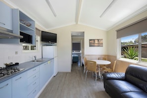 A compact kitchen with a gas stove, microwave, and refrigerator, leading to a dining area with a table and chairs. - Reflections Holiday Parks Scotts Head (Scotts Head)