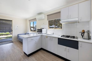A modern kitchen with white cabinets, a microwave, a gas stove, and a sink. - Reflections Holiday Parks Scotts Head (Scotts Head)
