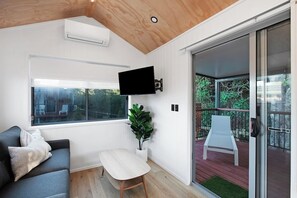 A modern living room with a flat-screen TV, a sofa, a small table, and a sliding glass door leading to an outdoor deck. - Reflections Holiday Parks Scotts Head (Scotts Head)
