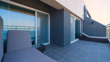 A modern outdoor lounge area with a glass balustrade, a cushioned seating area, and a clear view of the sky.