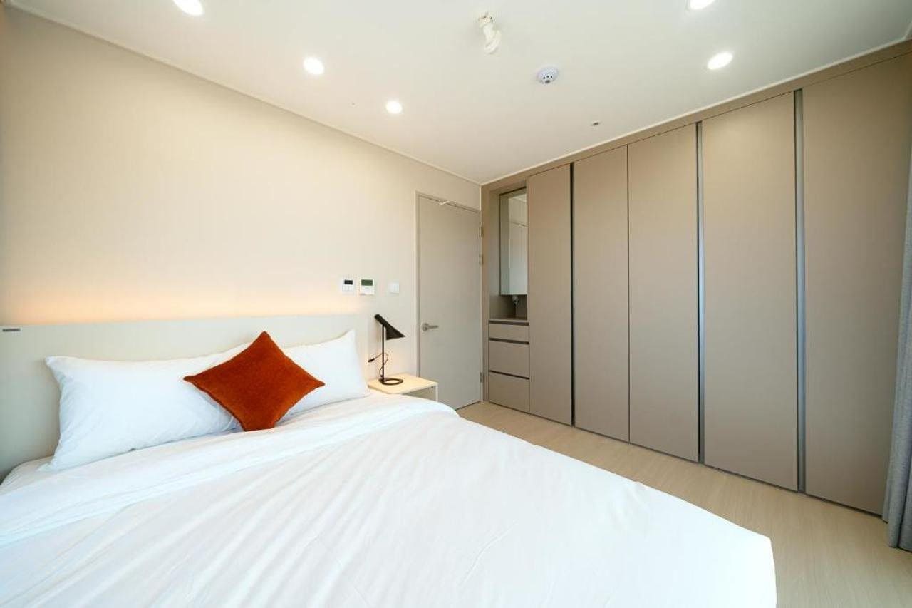 A modern bedroom with a large bed, a bedside table, a nightstand, a wardrobe, and a mirror.