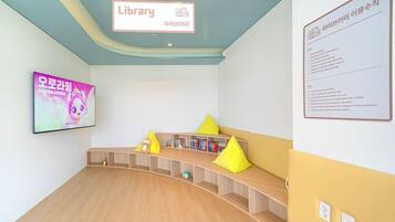 A children's library with a wooden bench, bookshelves, and a television displaying a cartoon.