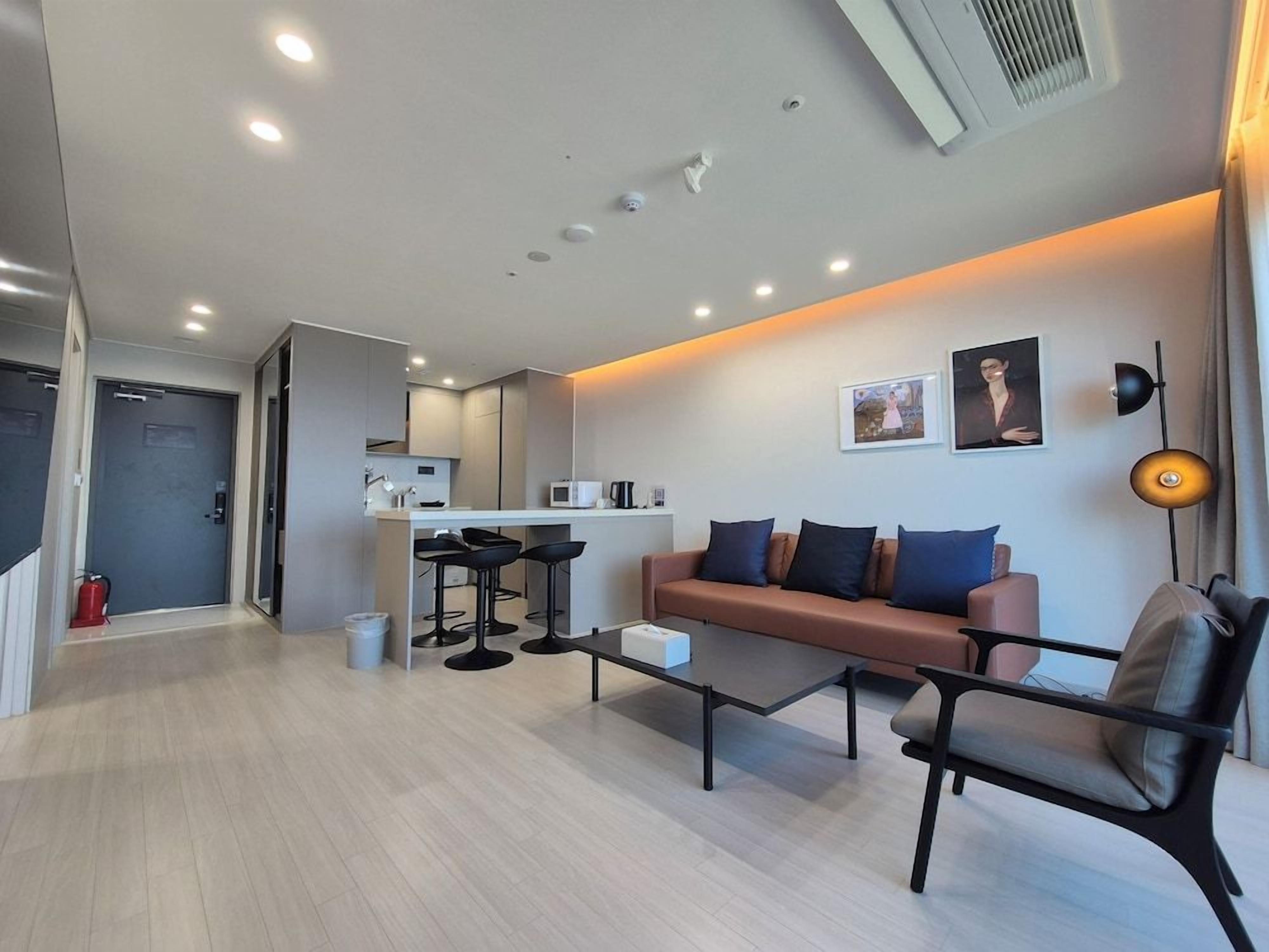 A modern living room with a sofa, a coffee table, and a dining area with a kitchen in the background.