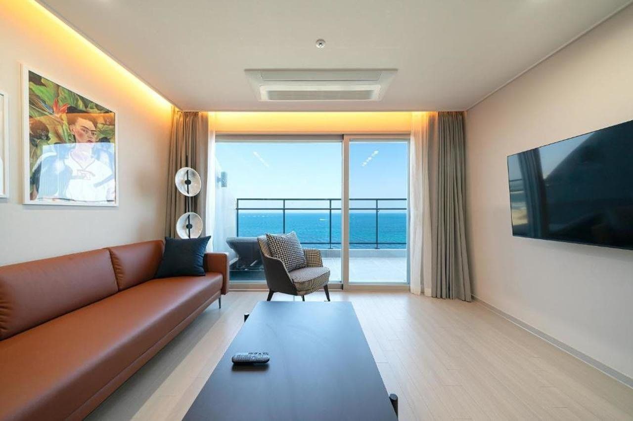 Una habitación de hotel moderna con sofá, sillón y una amplia pantalla de televisión.
