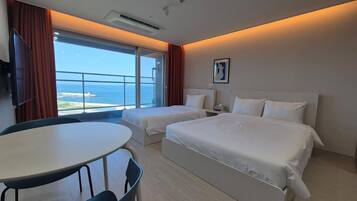 A hotel room with two beds, a dining table, and a view of the sea.