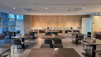 Una sala de conferencias moderna con mesas y sillas, una zona de cocina con electrodomésticos y un gran ventanal que proporciona luz natural.