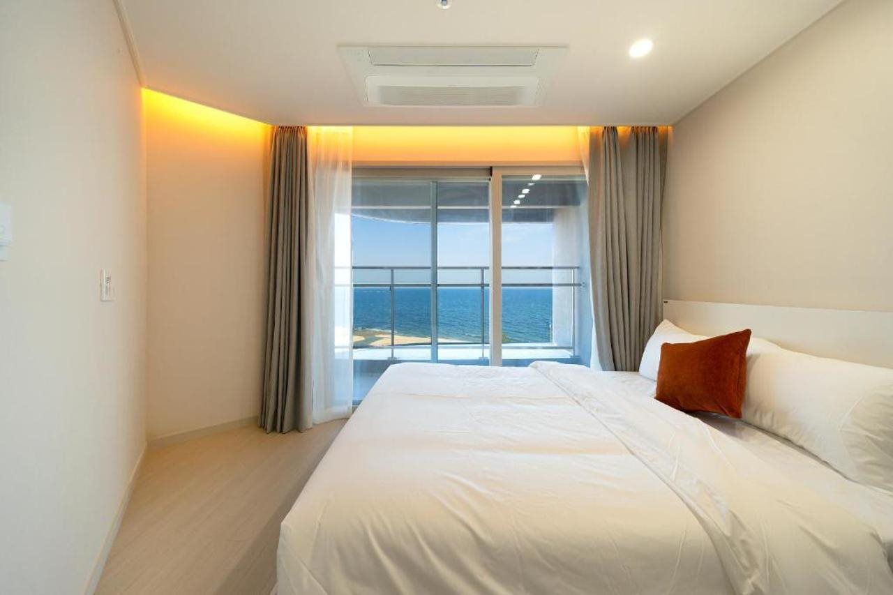 Una habitación de hotel con una cama grande, vista al mar y un balcón con cortinas.