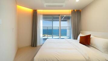 Una habitación de hotel con una cama grande, vista al mar y un balcón con cortinas.