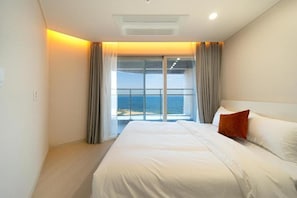 Ein Hotelzimmer mit einem großen Bett, Meerblick und einem Balkon mit Vorhängen.