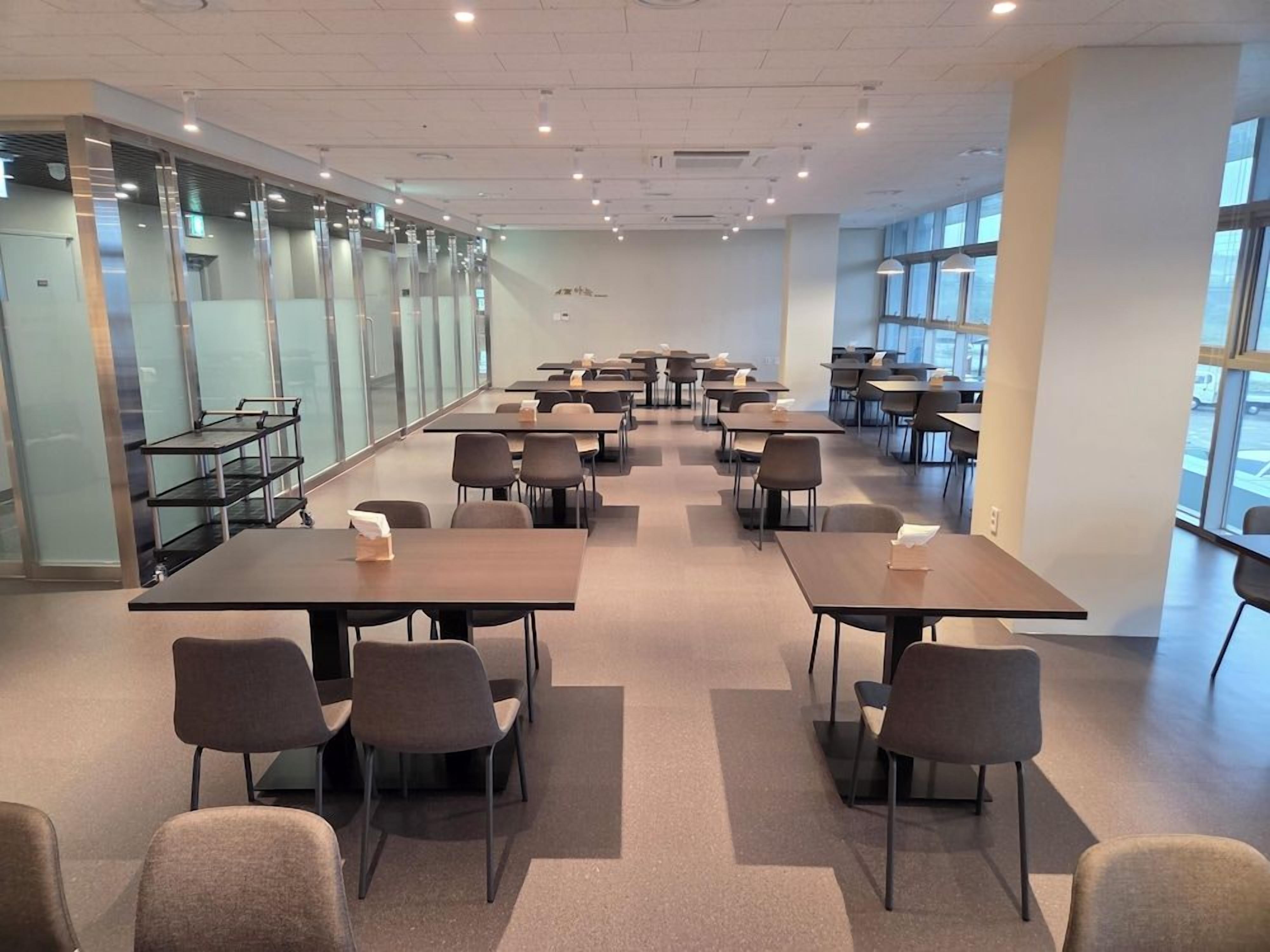 Una espaciosa sala de conferencias con múltiples mesas y sillas, amplias ventanas y un diseño de interiores moderno.