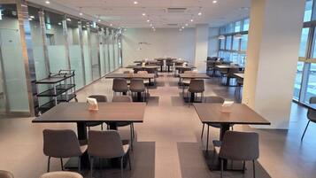 Una espaciosa sala de conferencias con múltiples mesas y sillas, amplias ventanas y un diseño de interiores moderno.