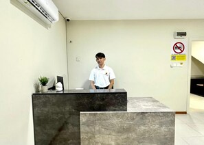 A reception desk with a person standing behind it, a no-smoking sign, and a QR code on the wall. - Swing & Pillows at Salak Tinggi Klia Transit (Sepang)