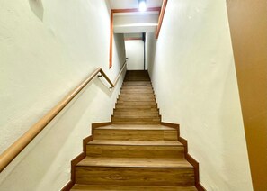 En trätrappa med ett ledstång, som leder uppåt i en smal hall med enkla väggar.