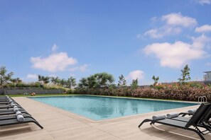 A swimming pool with lounge chairs, surrounded by greenery and a clear sky. - Courtyard by Marriott Dakar Diamniadio (Dakar)