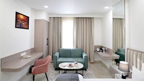 Una habitación de hotel moderna con un sofá, una silla, una mesita, una cama, una mesita de noche, un espejo y una ventana con cortinas.