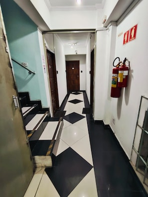 A hallway with a black and white tiled floor, a fire extinguisher mounted on the wall, and a door at the end.