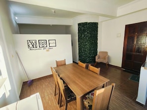 A dining area with a wooden table and chairs, a decorative wall with greenery, and a door in the background.