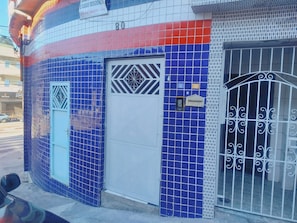 A building facade with a blue-tiled entrance, a white door, and a metal gate.