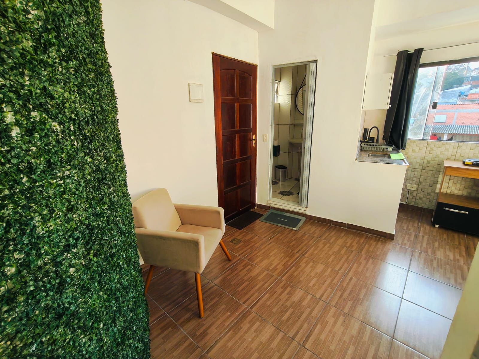 Una habitación con puerta de madera, una silla, una mesita y un ventanal con cortinas.