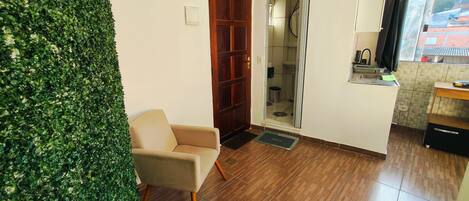 Una habitación con puerta de madera, una silla, una mesita y un ventanal con cortinas.
