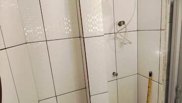 Casa de banho com paredes revestidas de azulejos brancos, sanita, chuveiro com duche manual e janela.