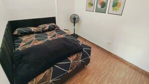 Makuuhuone, jossa on sänky, lattiatuuletin ja kolme abstraktia seinätaideteosta.