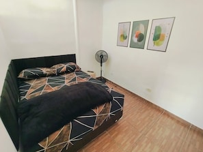 Un dormitorio con cama, un ventilador de pie y tres obras de arte abstractas en la pared.