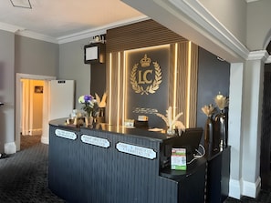 Un comptoir d’accueil d’hôtel avec un revêtement en bois foncé, un emblème en forme de couronne et un panneau indiquant un tarif de 150 $ par nuit.