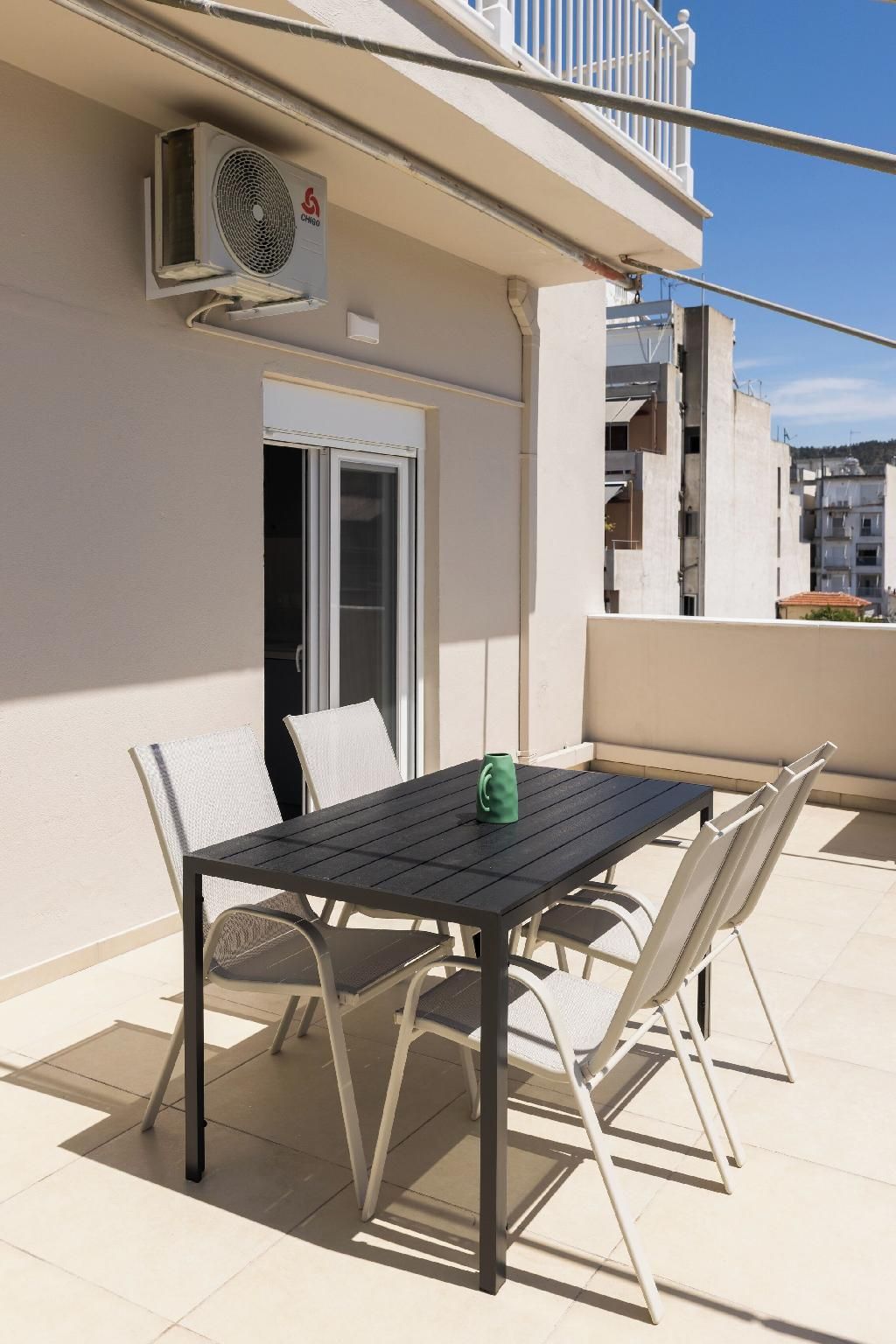 A balcony with a table and chairs, an air conditioning unit, and a door.