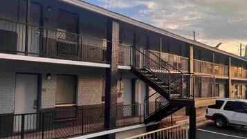 A multi-story motel with a central staircase, a parking lot, and a clear sky.