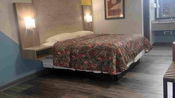 A hotel room with a bed, a nightstand, a wall-mounted lamp, and a bathroom visible through an open door.