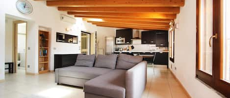 A modern living room with a sectional sofa, a kitchen in the background, and a wooden ceiling.