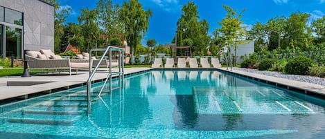 A clear swimming pool with lounge chairs and a modern building in the background.