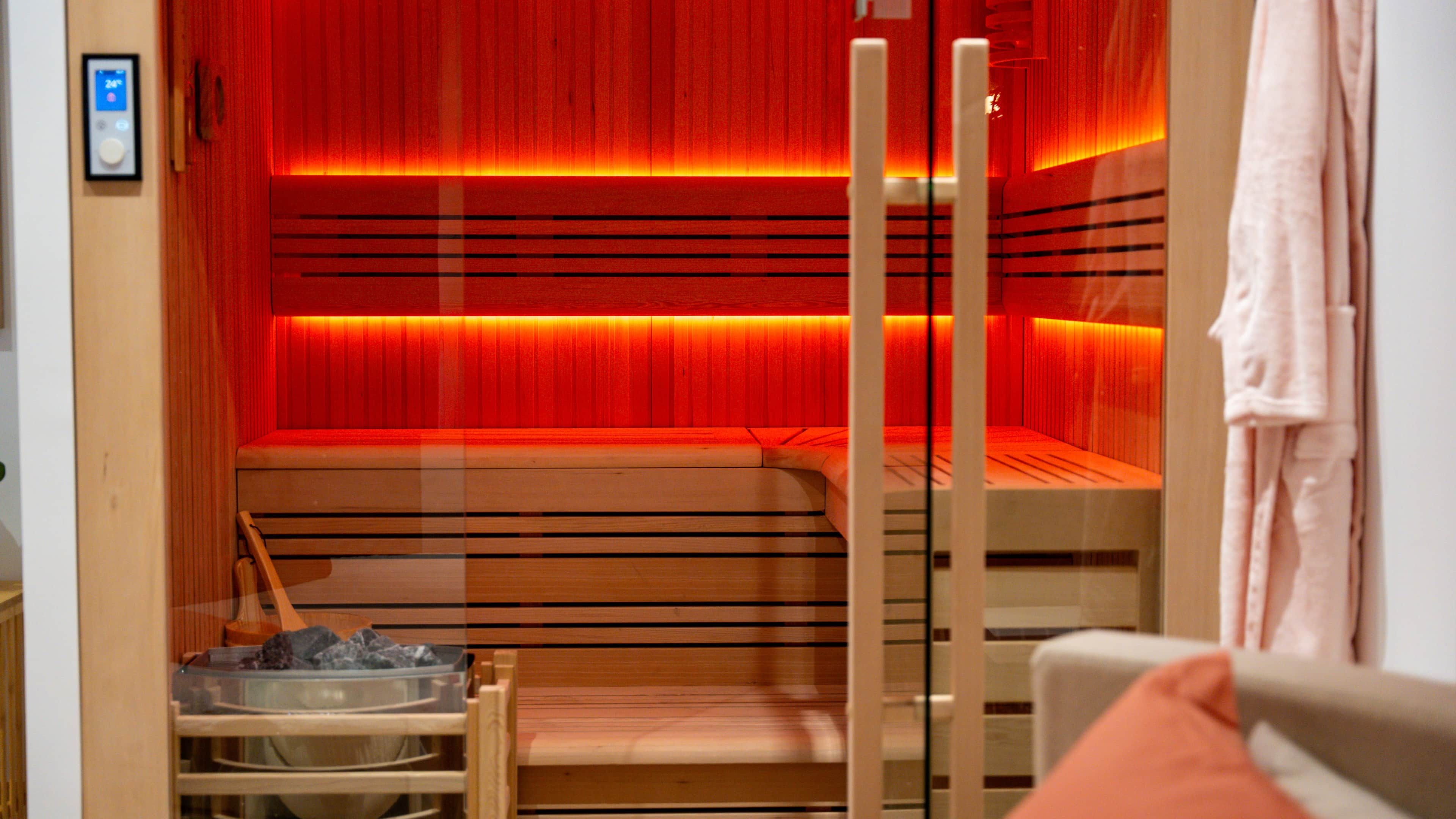 Una sauna con panche in legno, una porta in vetro, un portascopevoli e un pannello di controllo a parete.
