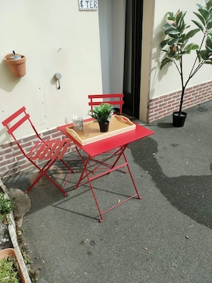 A red metal table and chairs set on a concrete surface, with a potted plant and a tray with a mug on the table.