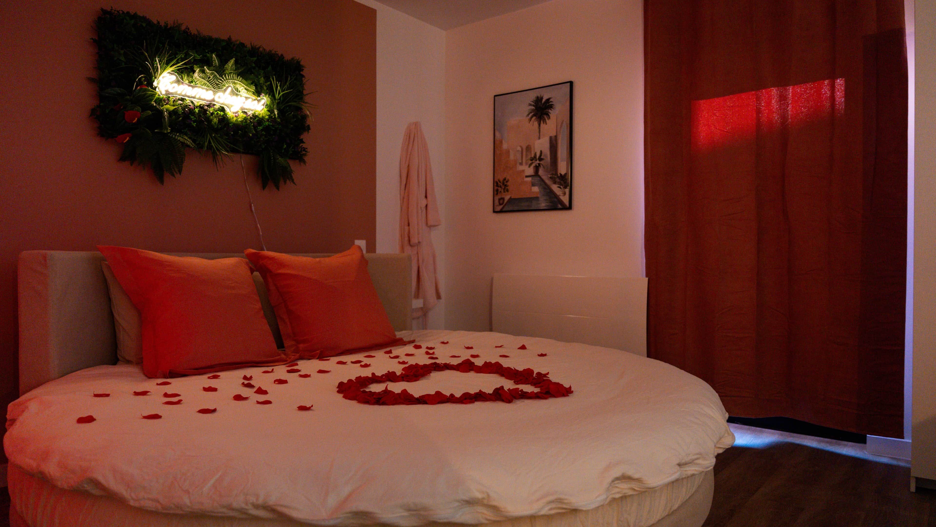 Ein Bett mit Rosenblättern, eine Wandleuchte und ein Gemälde.