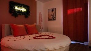 A bed with rose petals, a wall-mounted light, and a painting.