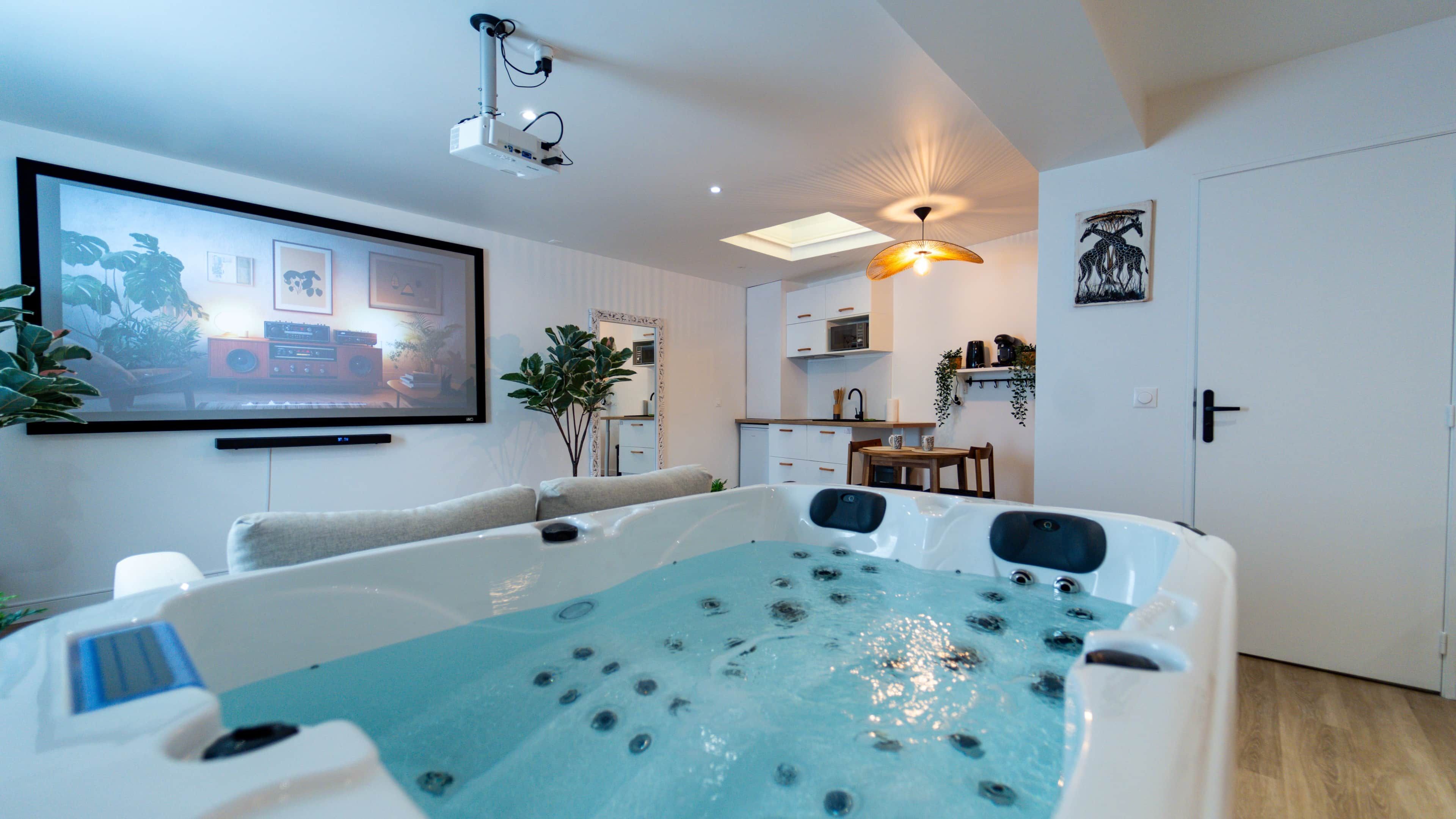 A modern living room with a large flat-screen TV, a seating area with a sofa, a hot tub, and a kitchen area in the background.