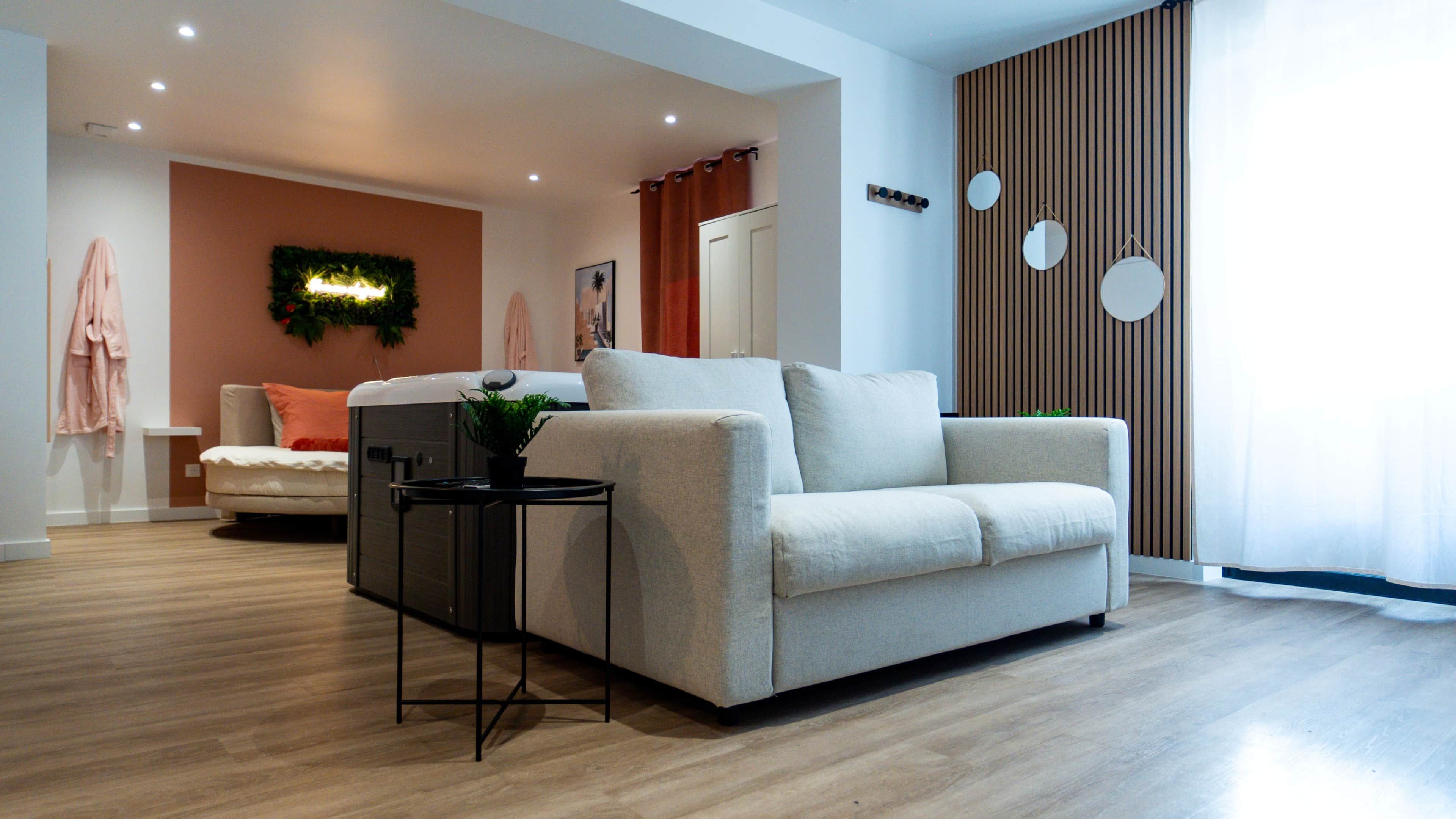 A modern living room with a sofa, a small table with a plant, and a wooden floor.