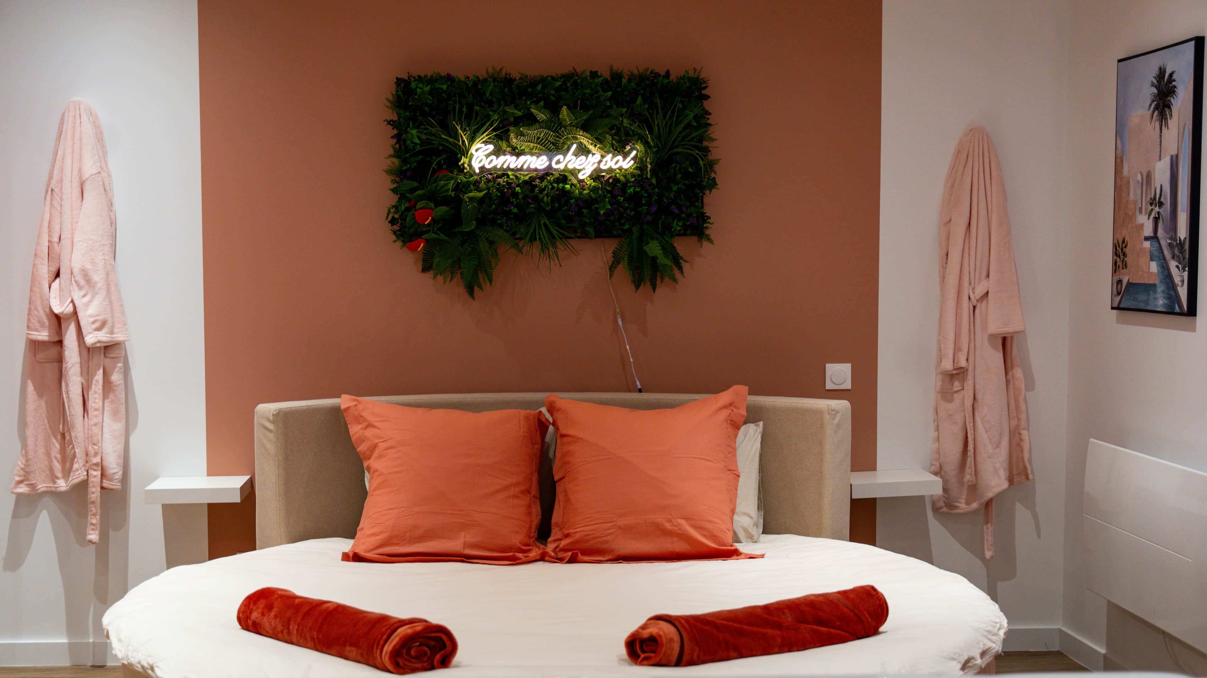 A hotel room with a bed, two pillows, a neon sign, and two towels.