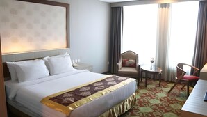 Una habitación de hotel con cama, una silla, una mesita y un ventanal con cortinas.