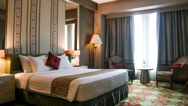 Una habitación de hotel con una cama grande, una silla, una mesita y una lámpara.