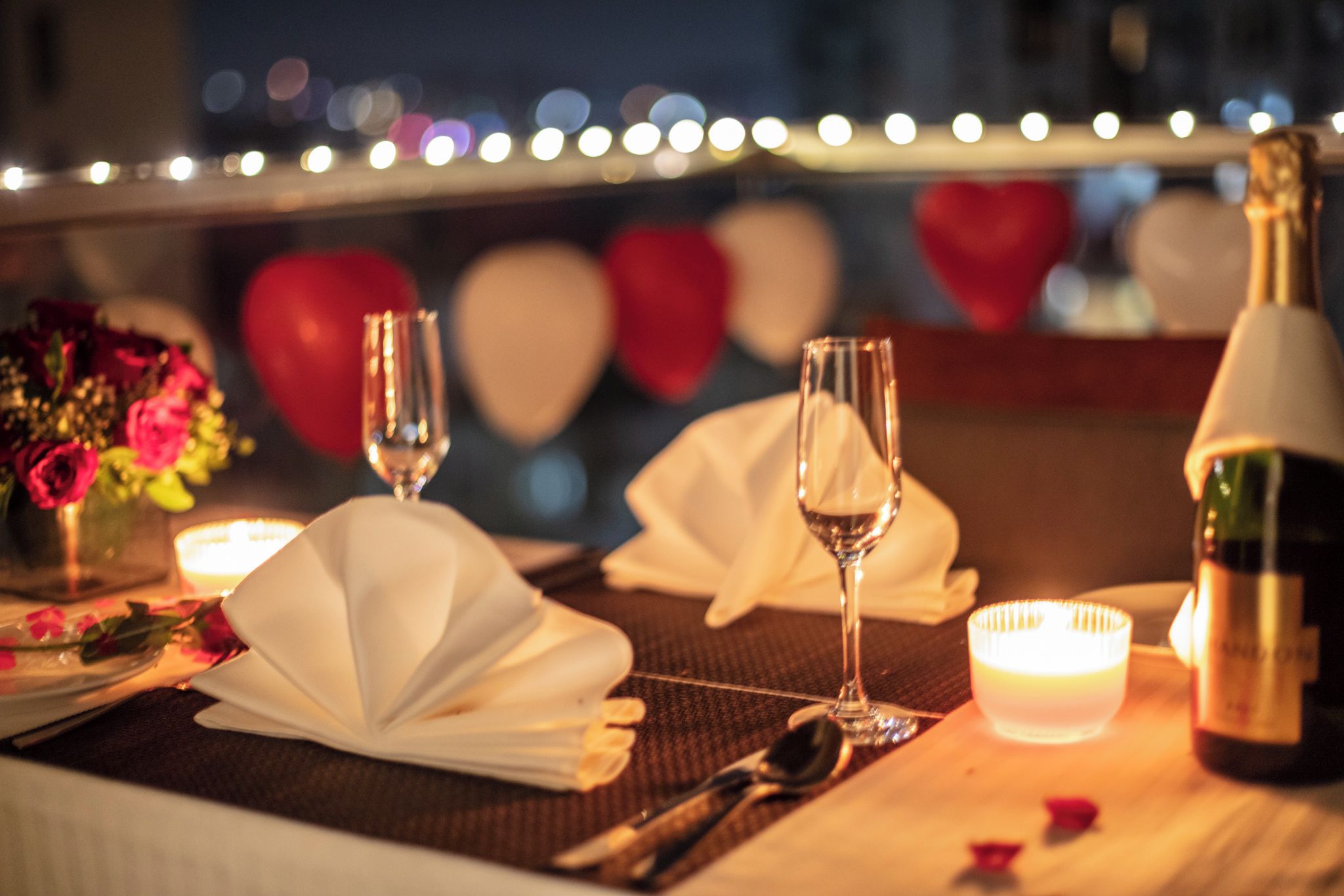 Un ambiente romántico para cenar, con una mesa dispuesta para dos, copas de vino, una botella de champán y una vela.