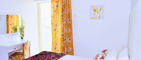 Une chambre d’hôtel avec un lit, un bureau, une chaise, une fenêtre avec des rideaux et un tableau au mur.