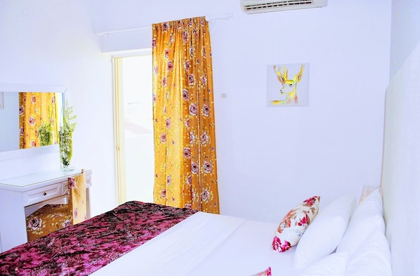 Quarto de hotel com cama, escrivaninha, cadeira, janela com cortinas e um quadro na parede.