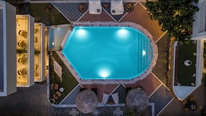 Vista aérea de uma piscina cercada por áreas de descanso, mobiliário de área externa e um jardim bem cuidado.