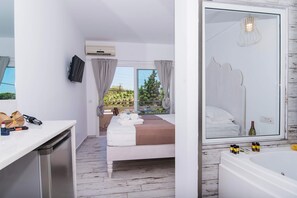 A hotel room with a bed, a bathroom, and a view of greenery outside. - Stella Maria Hotel & Suites (Hersonissos)