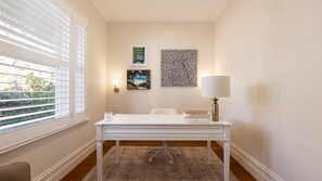Ein Zimmer mit einem weißen Schreibtisch, einer Lampe und Bildern an der Wand.