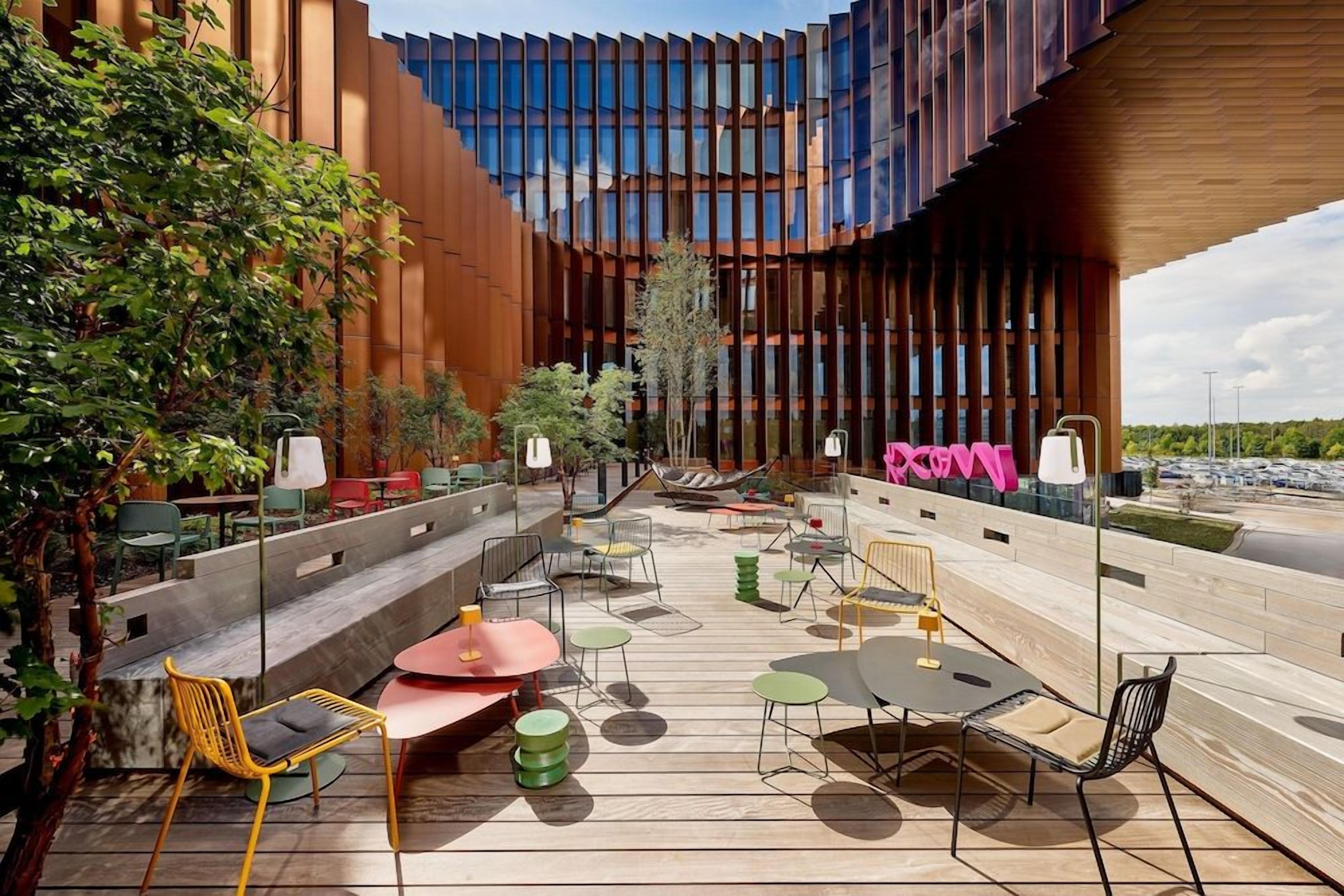 Een terras met verschillende stoelen en tafels, omgeven door een modern gebouw met grote ramen.
