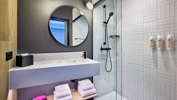 Ein modernes Badezimmer mit großem Spiegel, Waschbecken, Dusche und ordentlich gefalteten Handtüchern auf einem Regal.